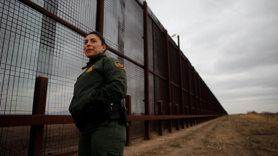 US border patrol agent stands next to the border fence separating the United States and Mexico.