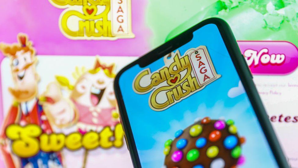 Smartphone displays Candy Crush Saga game and logo in background