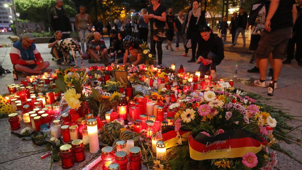 People lay flowers and candles at the spot where a German man was stabbed and later died of his injuries following an altercation