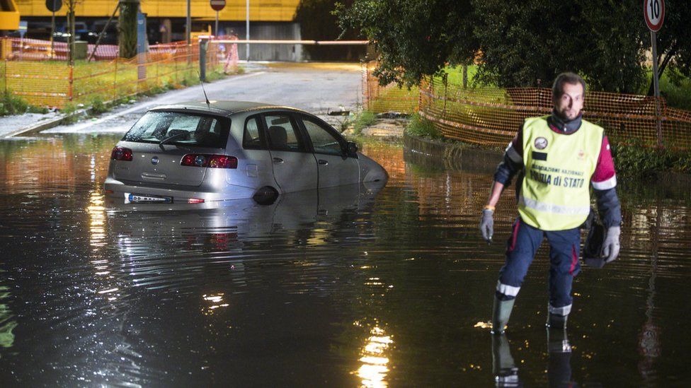 An Italian policeman wades in a flooded street near an abandoned car