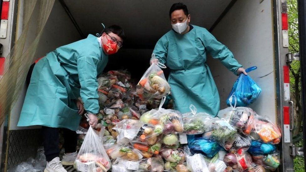 Рабочие в защитном снаряжении сортируют пакеты с овощами и продуктами на грузовике, чтобы раздать их жителям жилого комплекса во время карантина в Шанхае, 5 апреля