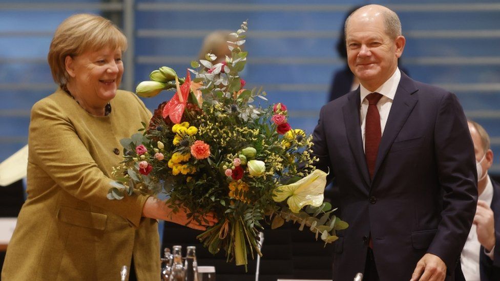 Исполняющая обязанности канцлера Германии Ангела Меркель получает букет от исполняющего обязанности министра финансов Германии Олафа Шольца перед еженедельным заседанием кабинета министров в канцелярии в Берлине, Германия, 24 ноября 2021 г.