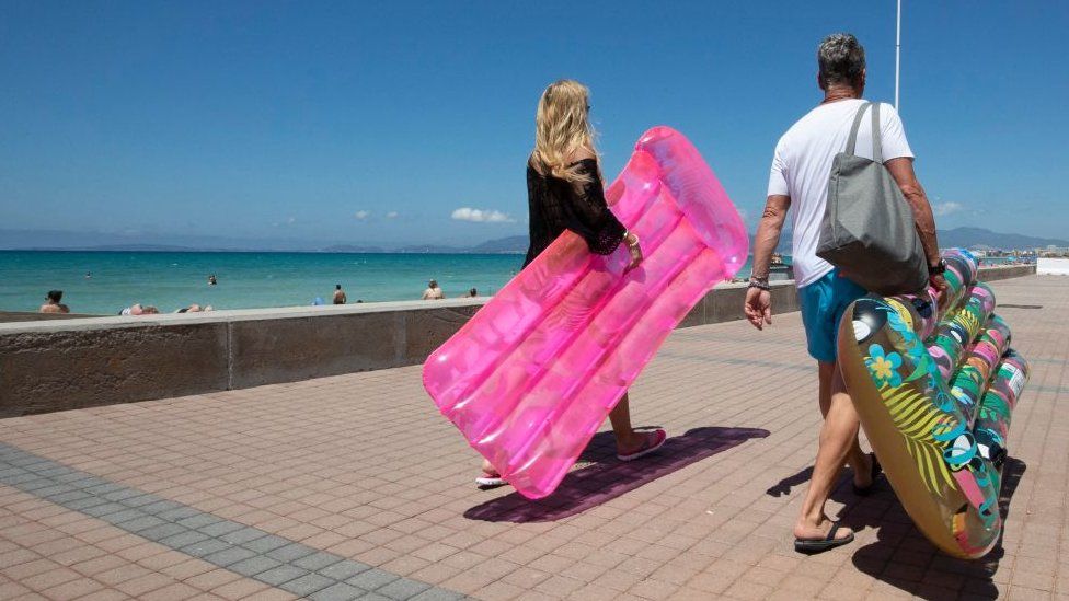 Tourists walk holding inflatable mattress at Palma Beach in Palma de Mallorca on June 7, 2021.