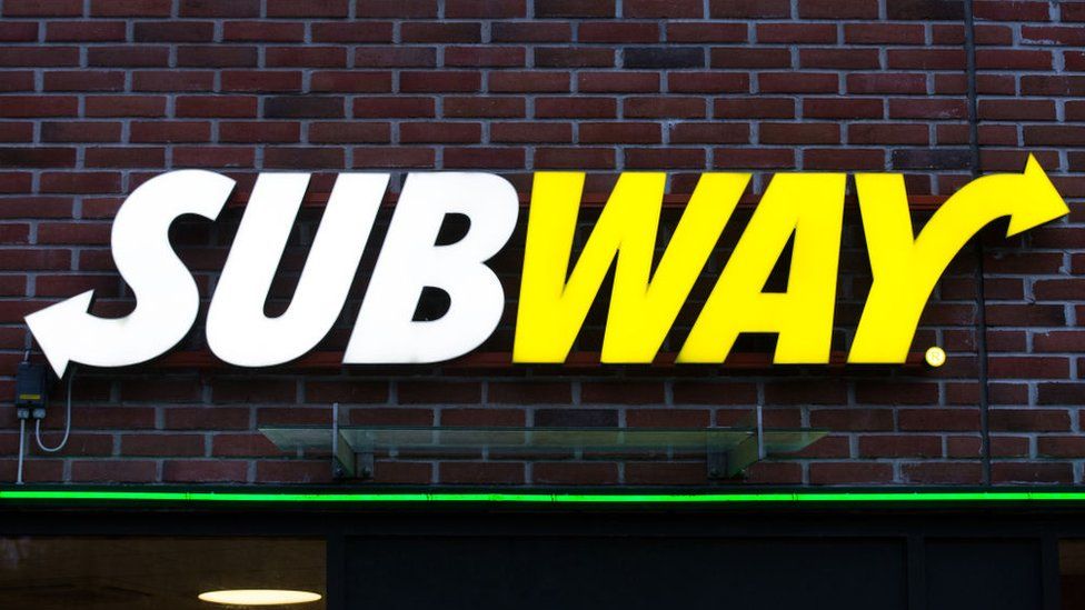 The Subway sandwich chain logo is seen bolted to a brick wall in this close-up shot
