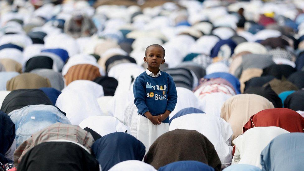 A boy standing ds in the middle of a crowd of people praying in the prostration position in Nairobi, Kenya.