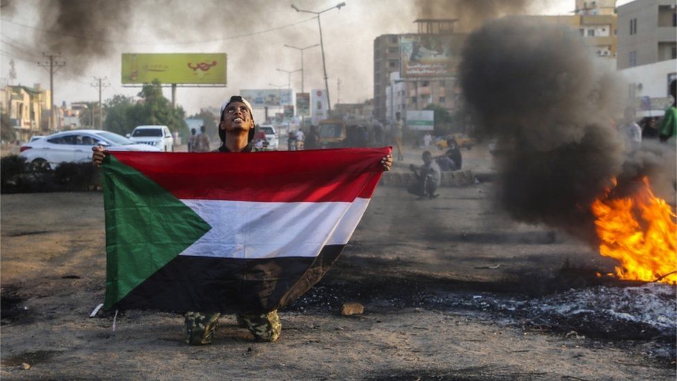 A Sudanese protester holds the national flag next to burning tyres during a demonstration in the capital Khartoum, Sudan, 26 October 2021