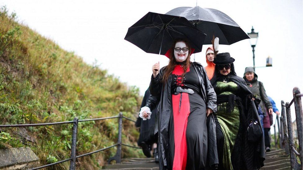 People dressed in gothic clothing walk down the steps from Whitby Abbey