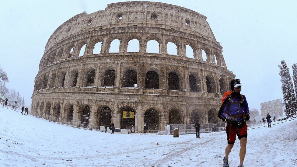 A man runs during heavy snowfall in front of the Colosseum in Rome