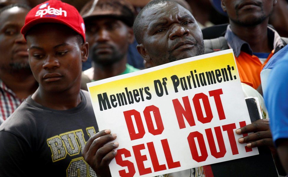 A protester outside parliament holds a sign reading: "Members of Parliament: Do not sell out!"