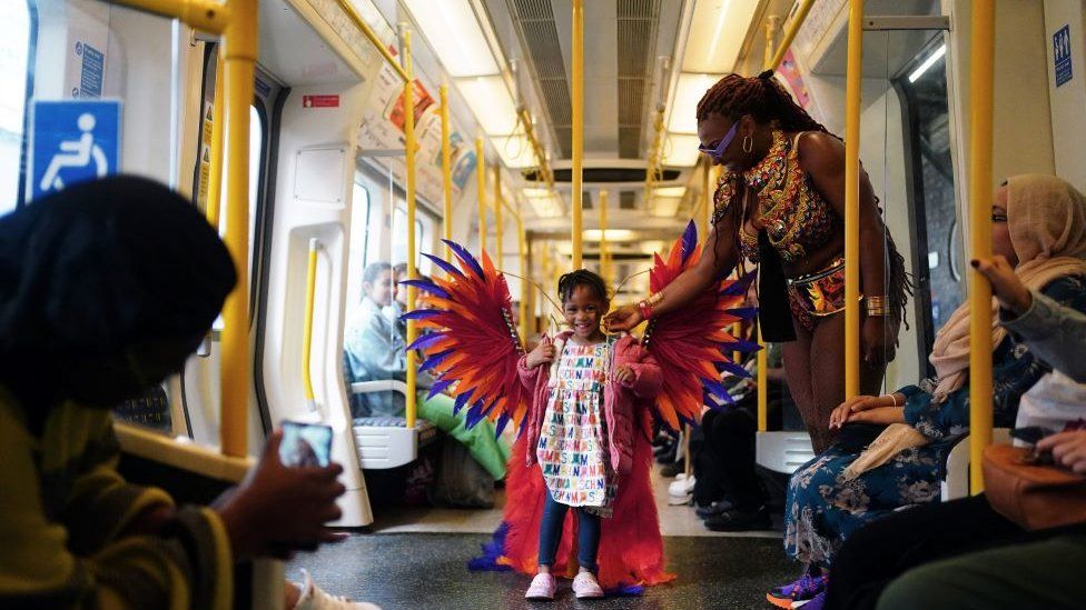 A young girl tries on a carnival goer's costume on the underground during the Notting Hill Carnival in London
