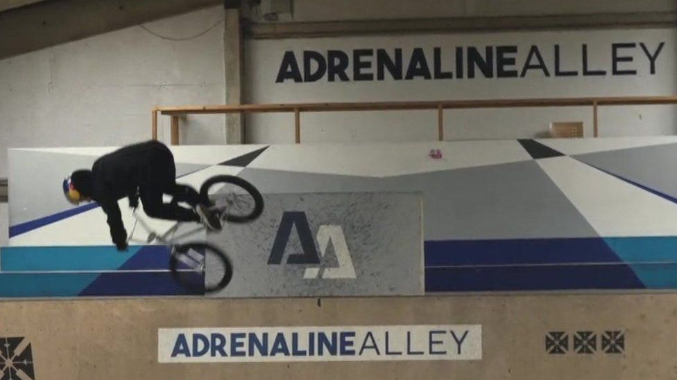 Kieran Reilly in black cycling gear wearing a helmet and just about to land back on the ramp