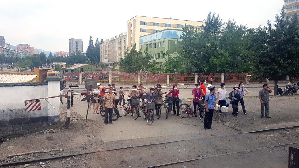 Masked citizens wait for a train to pass at a crossing in Phyongysong, North Korea