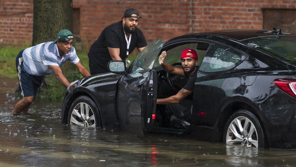 People push a car in floodwaters in New York