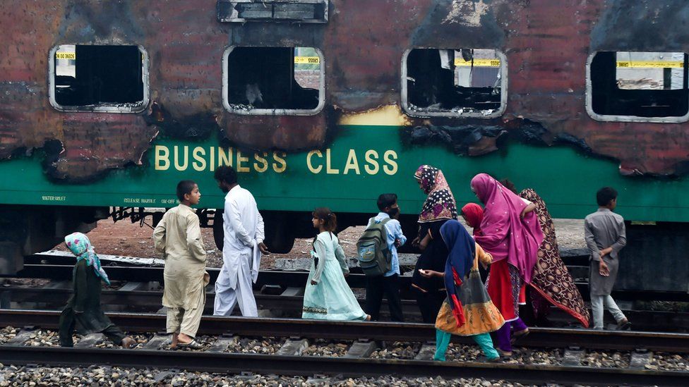 A family walks passed the charred remains of a train carriage