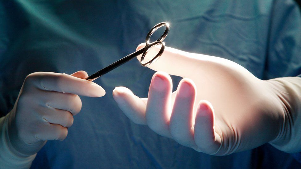 Nurse passing surgeon forceps during an operation