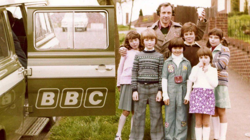 Andrew Sachs stops for a photo with local children during a BBC recording