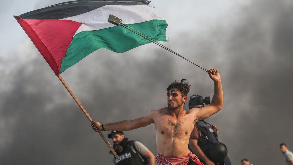 Palestinian holding a flag and swinging a sling