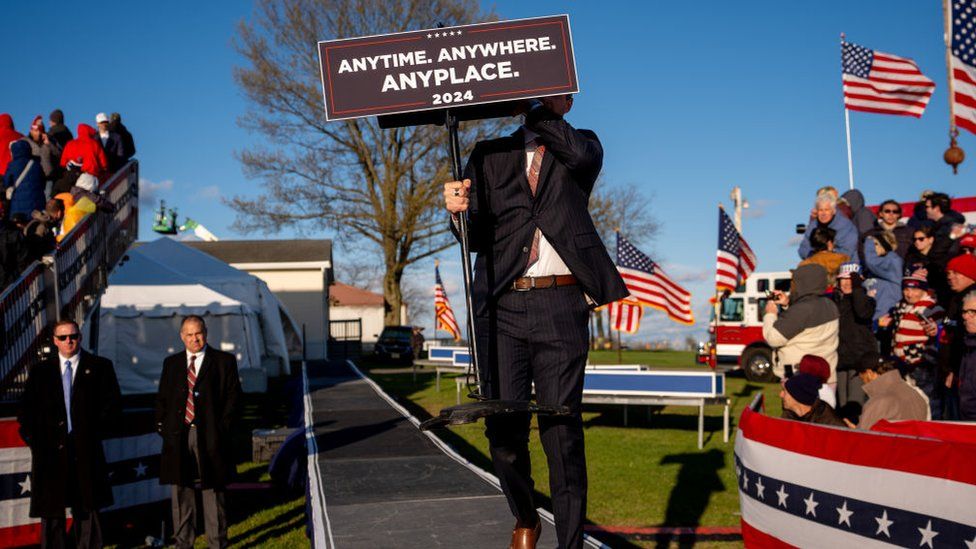An aide carries a podium that reads "Anytime. Anywhere. Anyplace" at a Pennsylvania rally