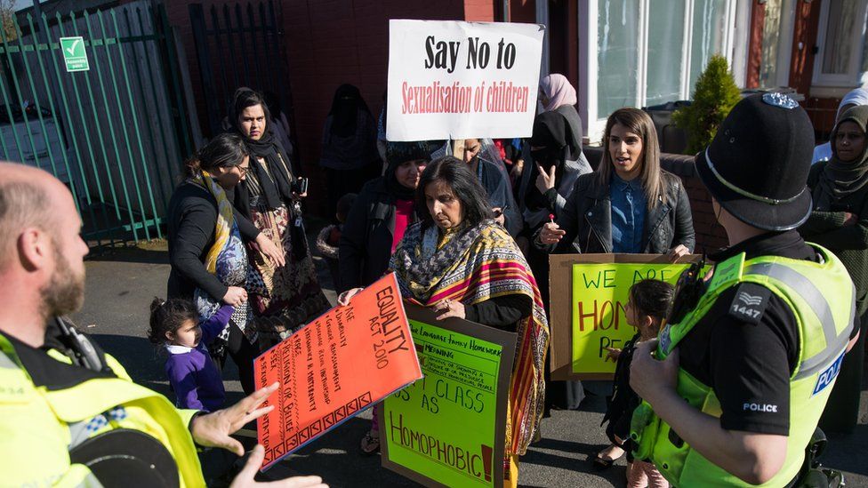 Police and parents at a protest outside a school. A placard reads "Say no to sexualisation of children"