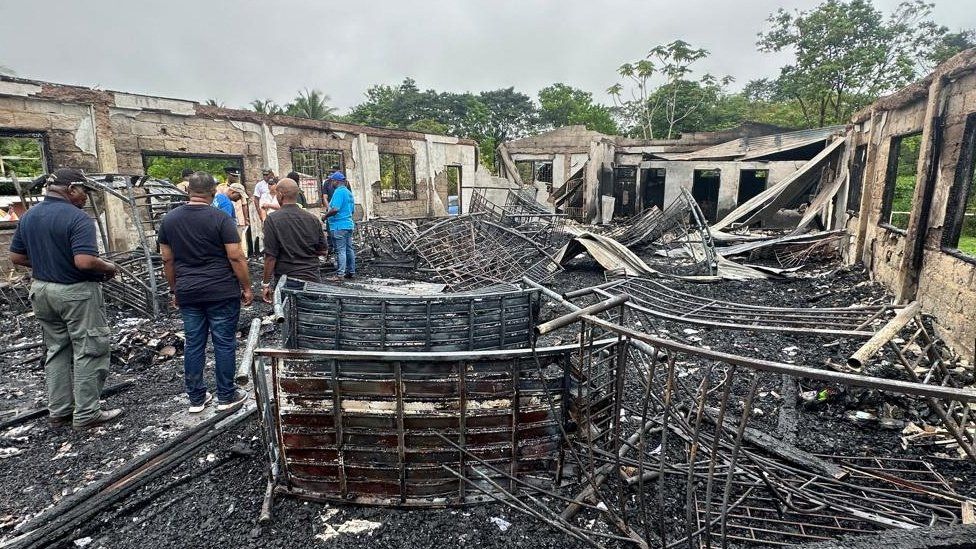 People stand inside the remains of a burnt secondary school dormitory in Guyana