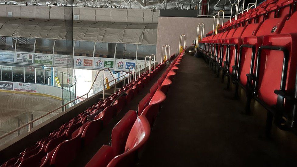 A picture of the empty ice rink seating with a corner of the rink.