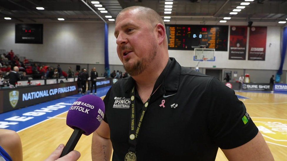 Man with very short hair wearing black tee-shirt and talking into a microphone