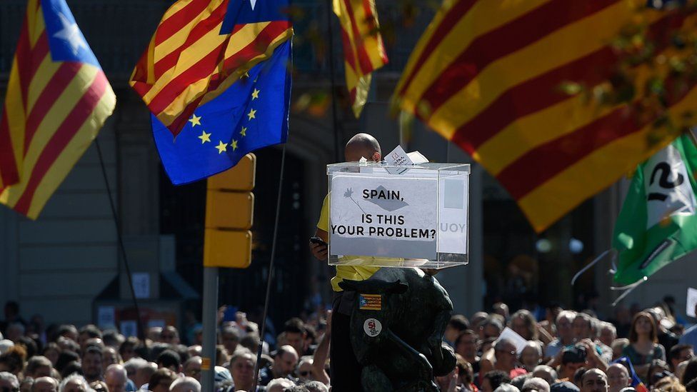 People in a large demonstration in Barcelona, holding Catalan flags and and a symbolic ballot box
