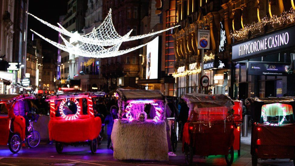 Night-time photo of illuminated pedicabs parked near London's Hippodrome casino on New year's Eve.
