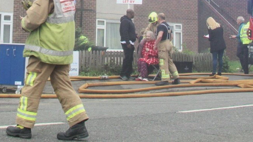 An elderly woman being looked after by emergency services after evacuation.
