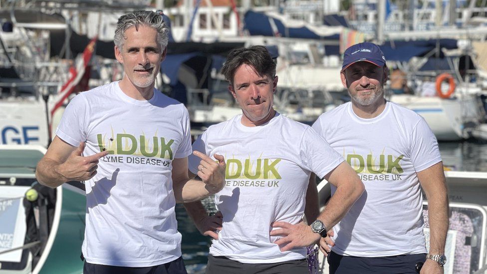 John Watling and two fellow rowers standing in a boat wearing Lyme disease T-shirts