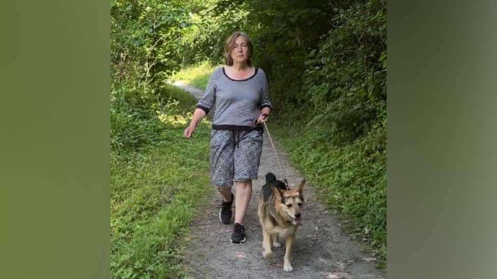 Sarah Robinson walking her dog Dylan in the Ironbridge Gorge, along a path flanked by trees