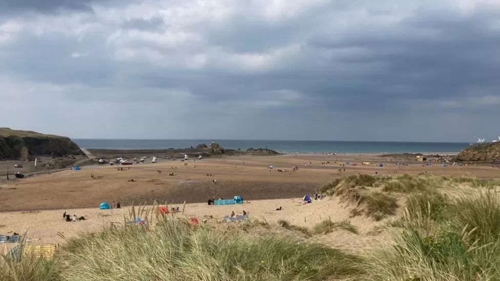 People enjoying a beach in Bude, with sand dunes in the foreground and the sea in the distance