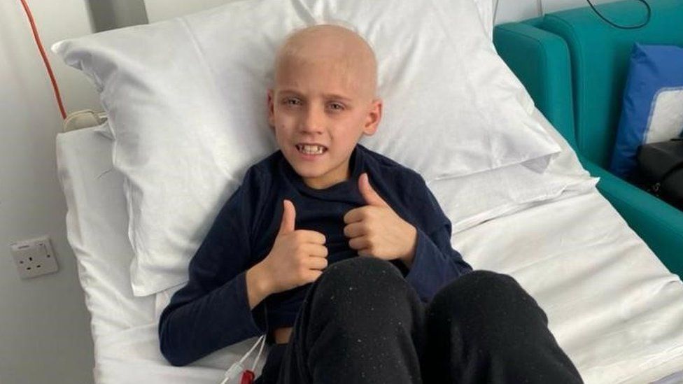 A boy in a hospital bed gives a thumbs up