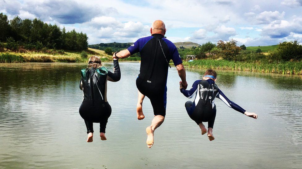 Family jump in a lake at Hundred House near Builth Wells, Powys