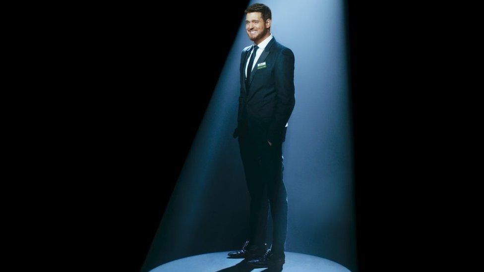 Michael Bublé in a black suit under a spotlight