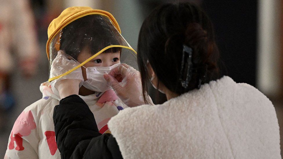 Женщина надевает маску на лицо ребенка в международном аэропорту Пекина.