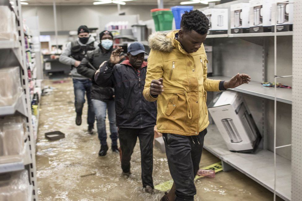 Suspected looters who surrendered to armed private security officers are marched outside, in a flooded mall in Vosloorus, on 13 July 2021