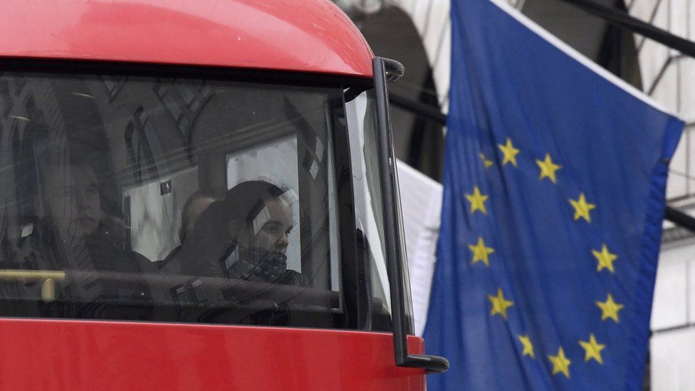 Passengers look out from a London bus as it passes an European Union flag in London.