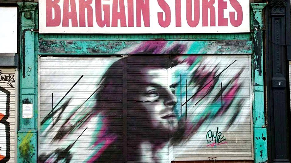 A sketchy graffiti portrait on shutters beneath a closed 'bargain store'