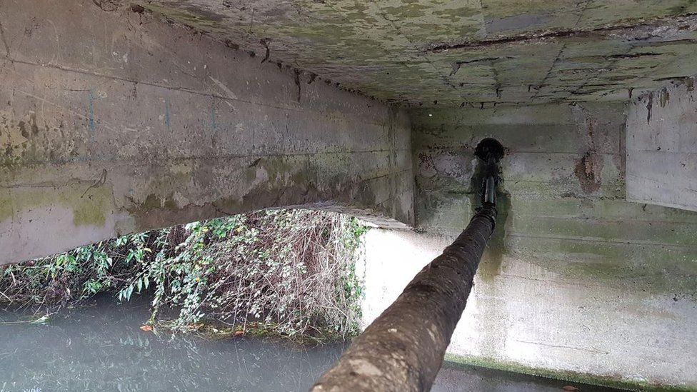 underneath of a bridge with rusty-looking pipe