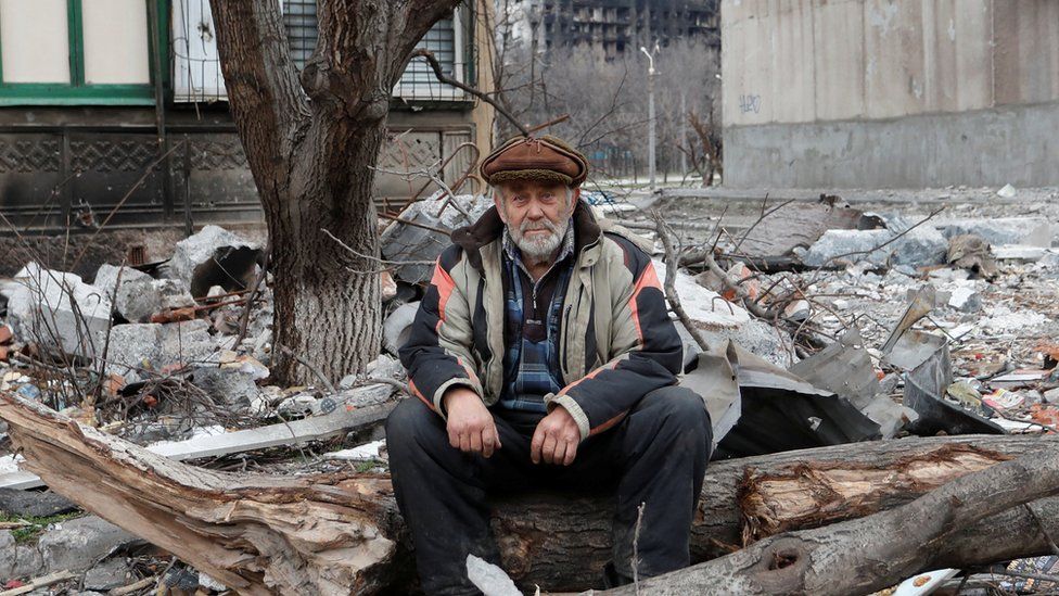 A local resident sits near a damaged apartment building in Mariupol