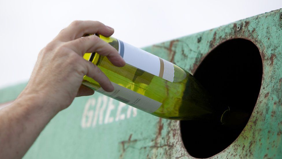Hand putting a wine bottle into a recycling bank