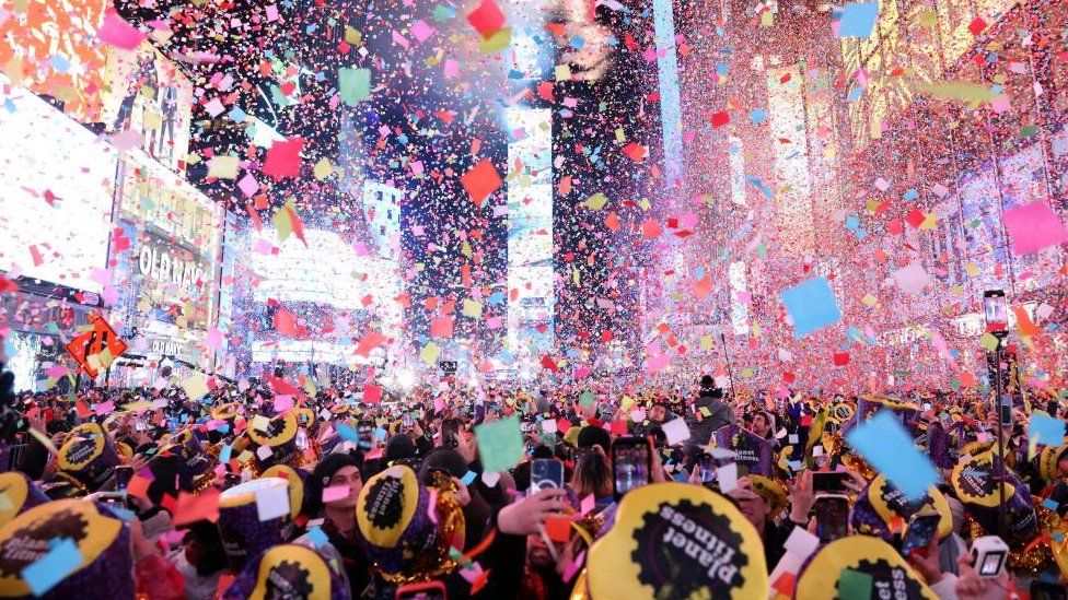 Конфетти летает вокруг часов обратного отсчета, охватывая людей, собравшихся на Таймс-сквер в Нью-Йорке, чтобы поприветствовать 2023 год