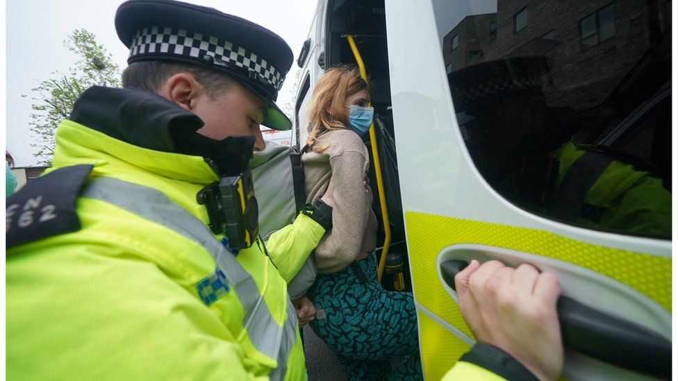 A police officer leads a woman into a police van