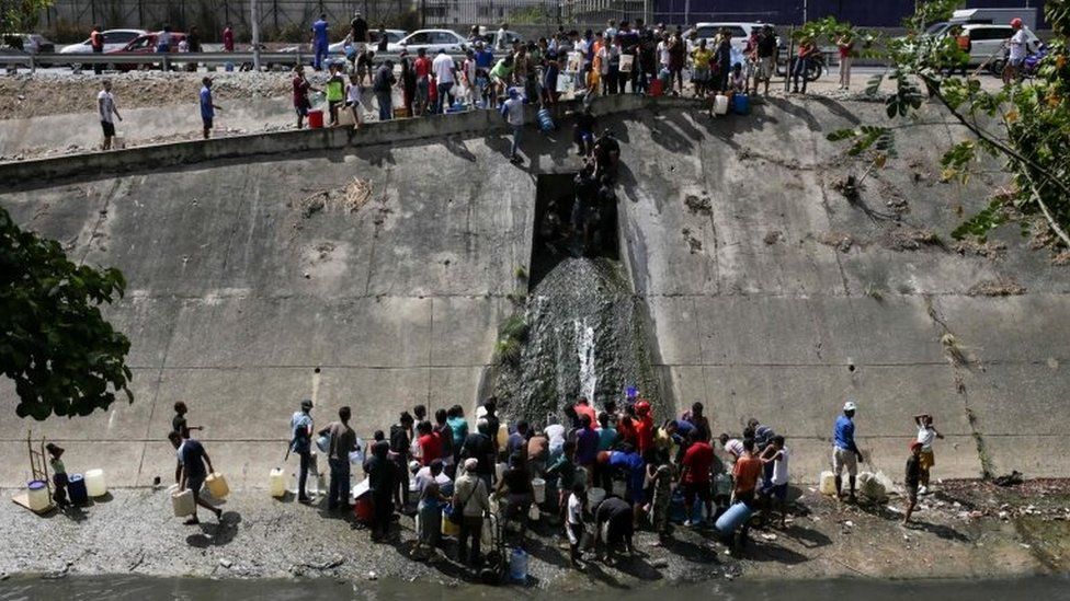 People collect water from a sewage canal at the river Guaire in Caracas on March 11, 2019,