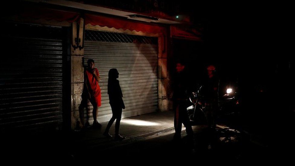 People use the light of a motorcycle to illuminate them as they talk on the street during a blackout in Caracas