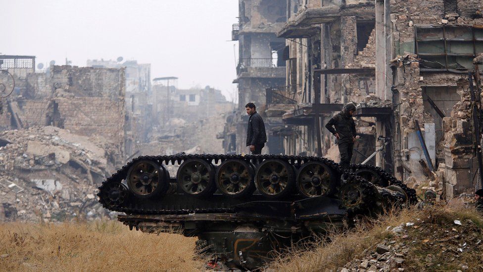 Forces loyal to Syria's President Bashar al-Assad stand atop a damaged tank near Umayyad mosque, in Aleppo, 13 December
