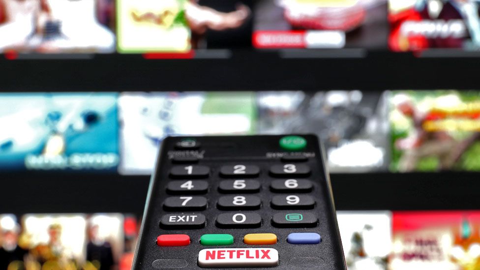 A TV remote control in front of a screen displaying Netflix