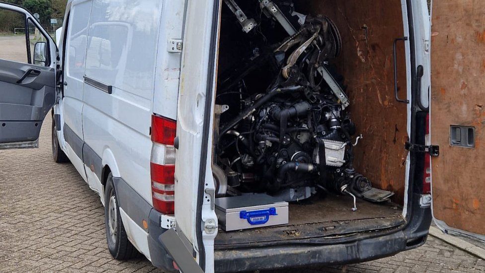 A tall white van with the rear doors open, revealing a pile of metalwork and plastics