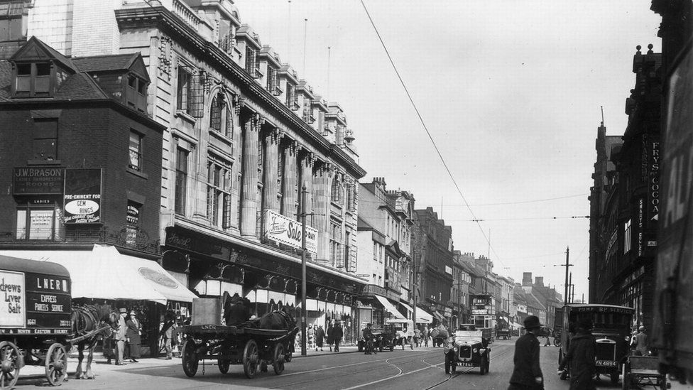 A black and white view of people and old cars on a street